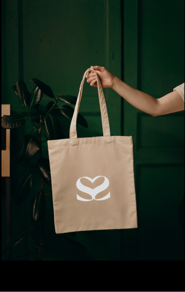 Main tenant un totebag beige avec le sigle valuesandco en blanc. Fond vert